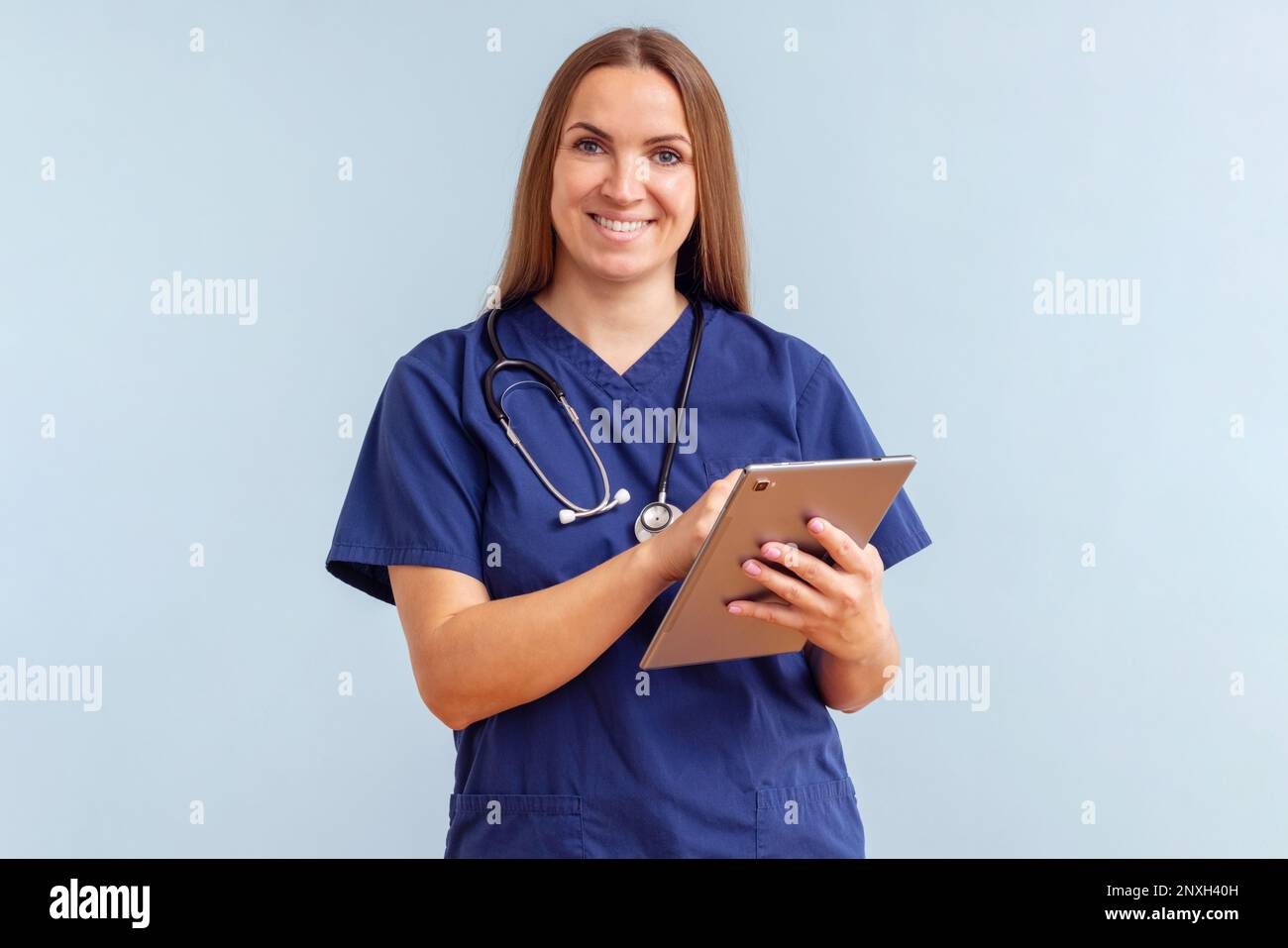 Lächelnde junge Ärztin arbeitet auf einem Tablet auf blauem Hintergrund Stockfoto