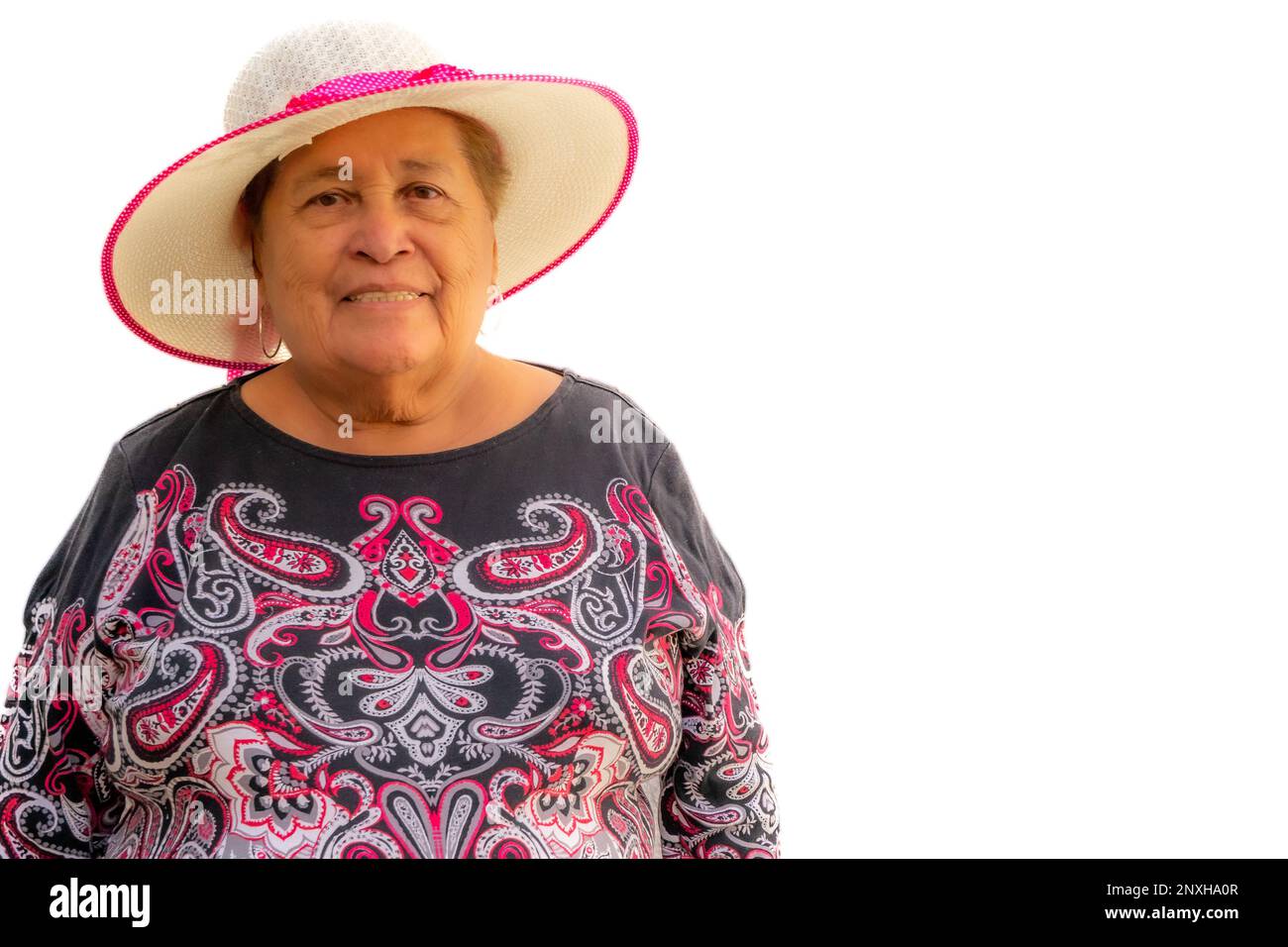 Schöne lächelnde ältere Frau mit kurzen Haaren, die einen Hut und eine schwarze Bluse mit pinkfarbenen Besätzen auf weißem Hintergrund trägt, in die Kamera schaut, enj Stockfoto