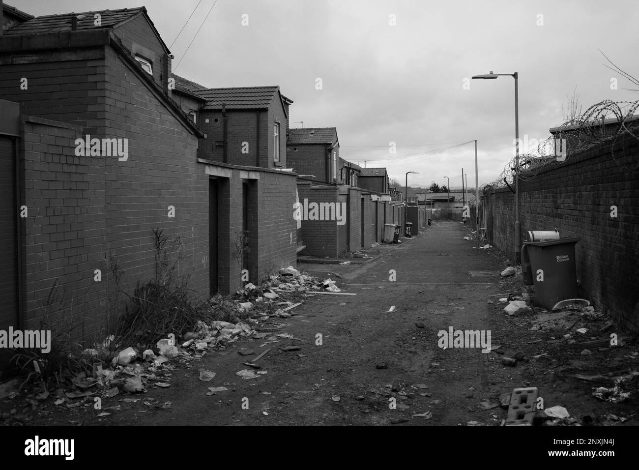 Typische britische „Hinterstraße“ in einer nördlichen Stadt mit Blick auf die Rückseite von Terrassenhäusern, mit viel Müll oder Abfall auf dem Boden. Bolton, England, Großbritannien Stockfoto
