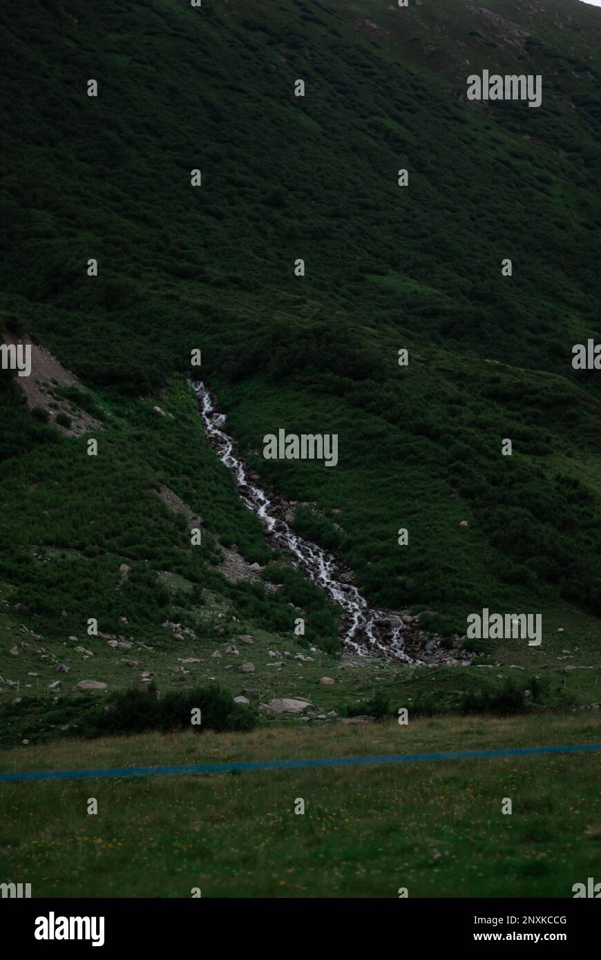 Blick auf den Wasserfall in der Nähe des Sees in den grünen Bergen der Alpen Stockfoto