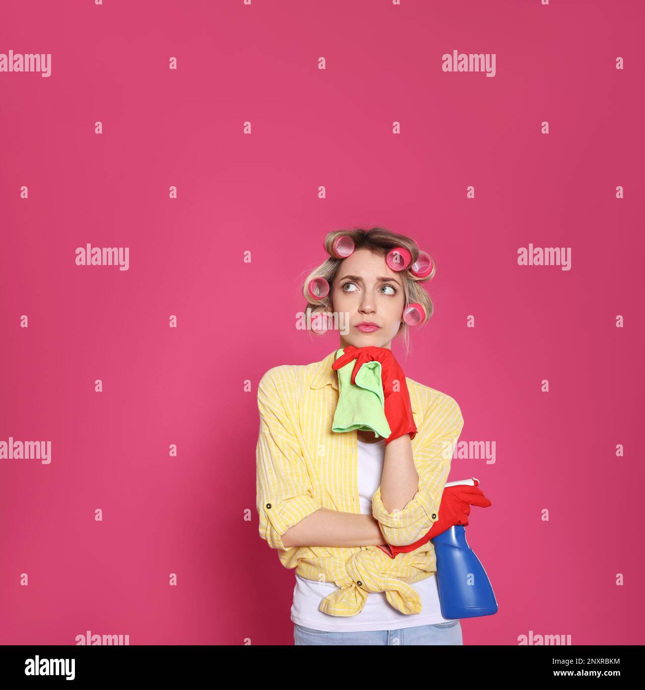 Junge Hausfrau mit Reinigungsmittel und Lappen auf rosa Hintergrund Stockfoto