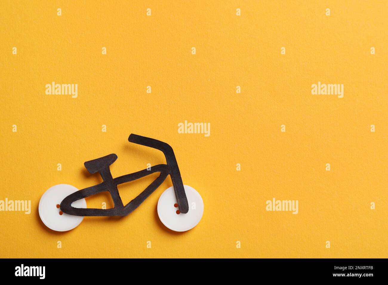 Fahrrad mit Knöpfen und schwarzem Papierausschnitt auf orangefarbenem Hintergrund, flach verlegt. Platz für Text Stockfoto