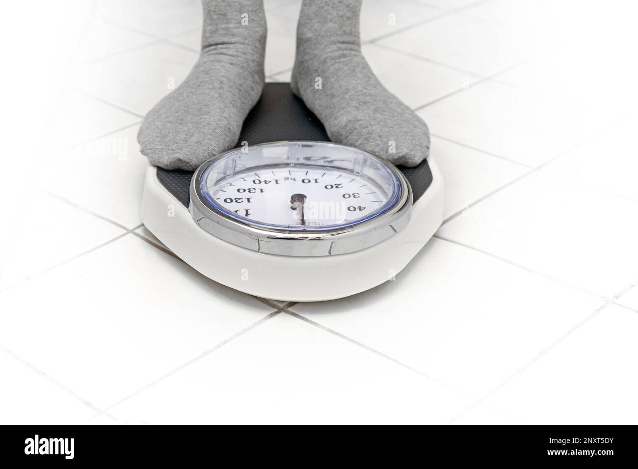 Füße in grauen Socken stehen auf einer persönlichen Waage auf dem weiß gefliesten Badezimmerboden für Gewichtsmessung, Kopierbereich, ausgewählten Fokus Stockfoto