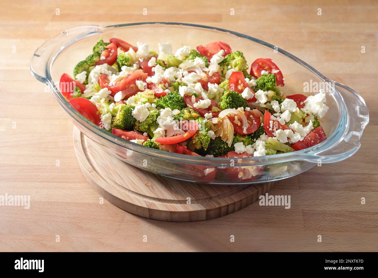 Gemüseauflauf mit Brokkoli, Tomaten, Zwiebeln und Fetakäse in einem für den Ofen zubereiteten Glasbackgericht, zubereitet eine vegetarische Mahlzeit, ausgewählt Stockfoto