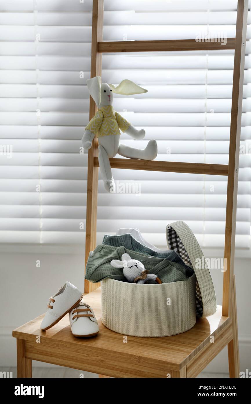 Box mit Babykleidung, Babyschühchen und Spielzeug auf einem Stuhl im Innenbereich Stockfoto