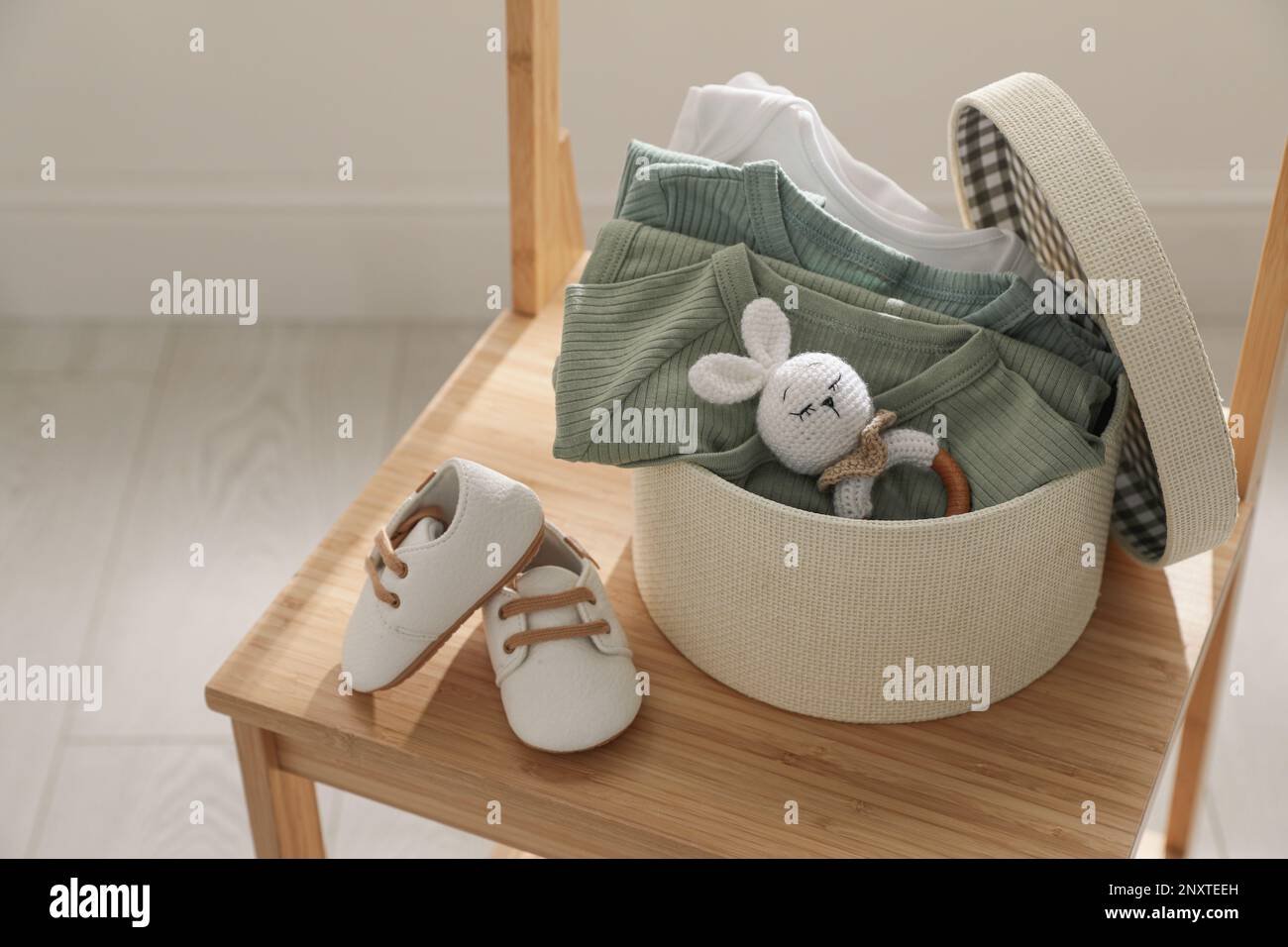 Box mit Babykleidung, Babyschühchen und Spielzeug auf einem Stuhl im Innenbereich Stockfoto