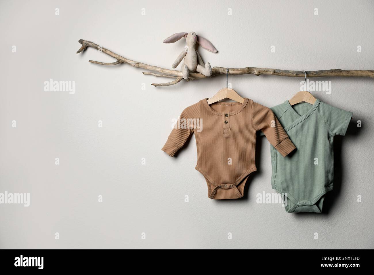 Babykleidung und Spielzeug auf einem Zierzweig in der Nähe einer hellen Wand. Platz für Text Stockfoto
