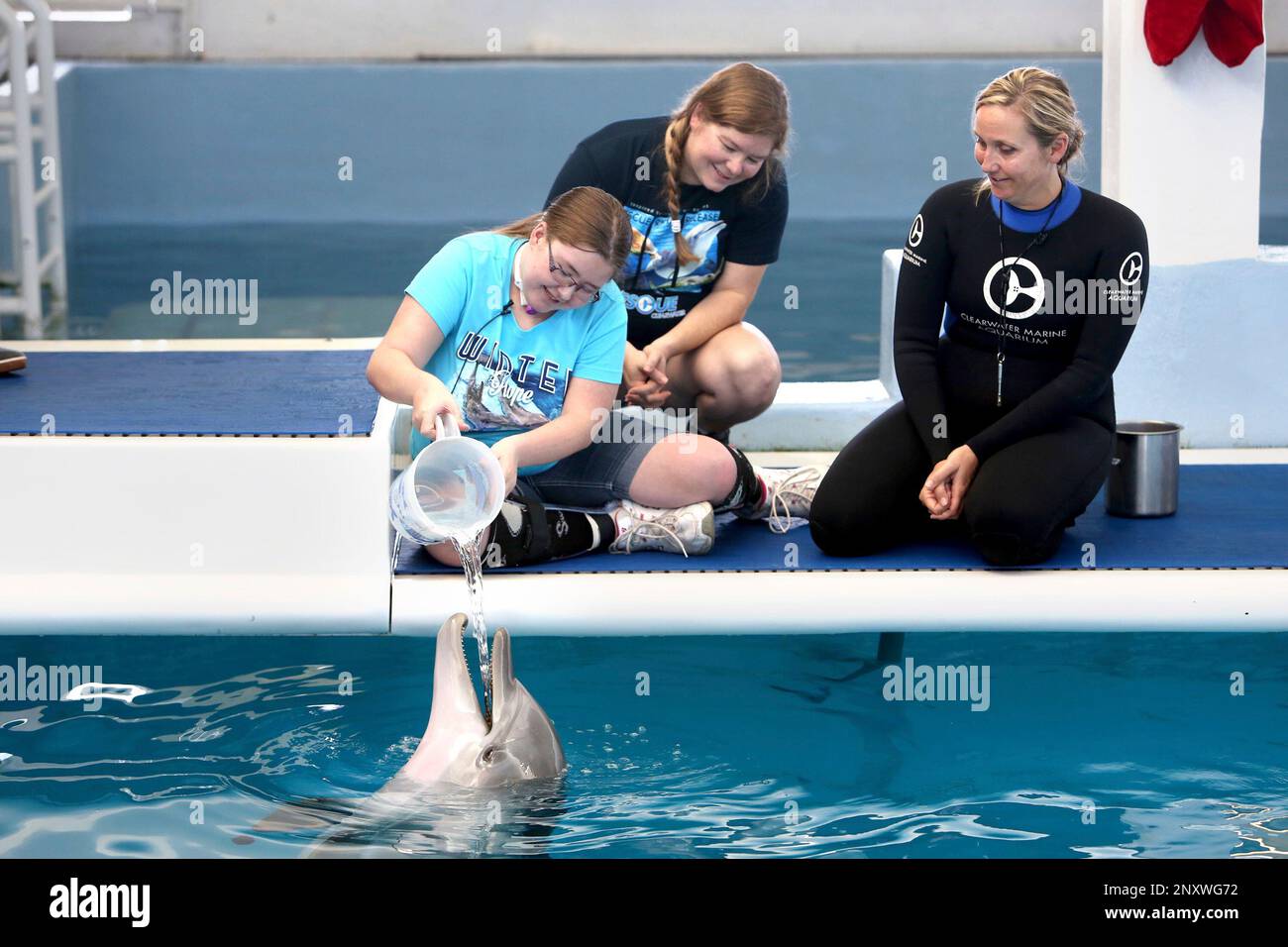 Autumn Swank, 18, of Joshua, Texas, left, offers water to Hope (the rescue dolphin) while visiting the Clearwater Marine Aquarium on Tuesday, Dec. 19, 2017, in Clearwater, Fla. Next to Swank is her mother, Crystal Fenn, and dolphin trainer Cammie Zodrow. Swank was diagnosed with inoperable brain stem cancer in 2009. The aquarium used Autumn's visit to kick off their Winter and Autumns Hope campaign. (Douglas R. Clifford/The Tampa Bay Times via AP) Stockfoto