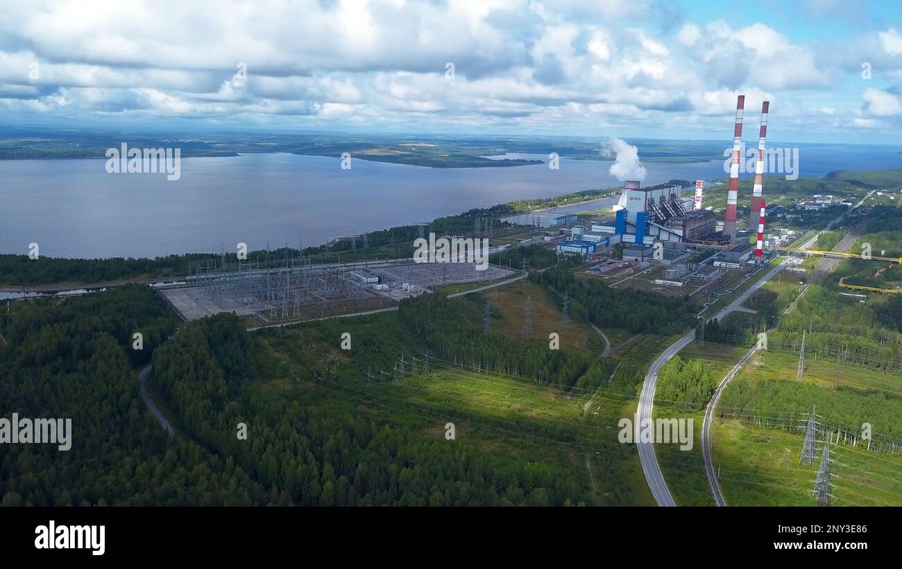 Draufsicht auf das Kraftwerk am Seeufer. Clip. Fabrikrohre vor dem Hintergrund von See und grünem Wald. Landschaft mit Kraftwerk und Rohren am See in s. Stockfoto
