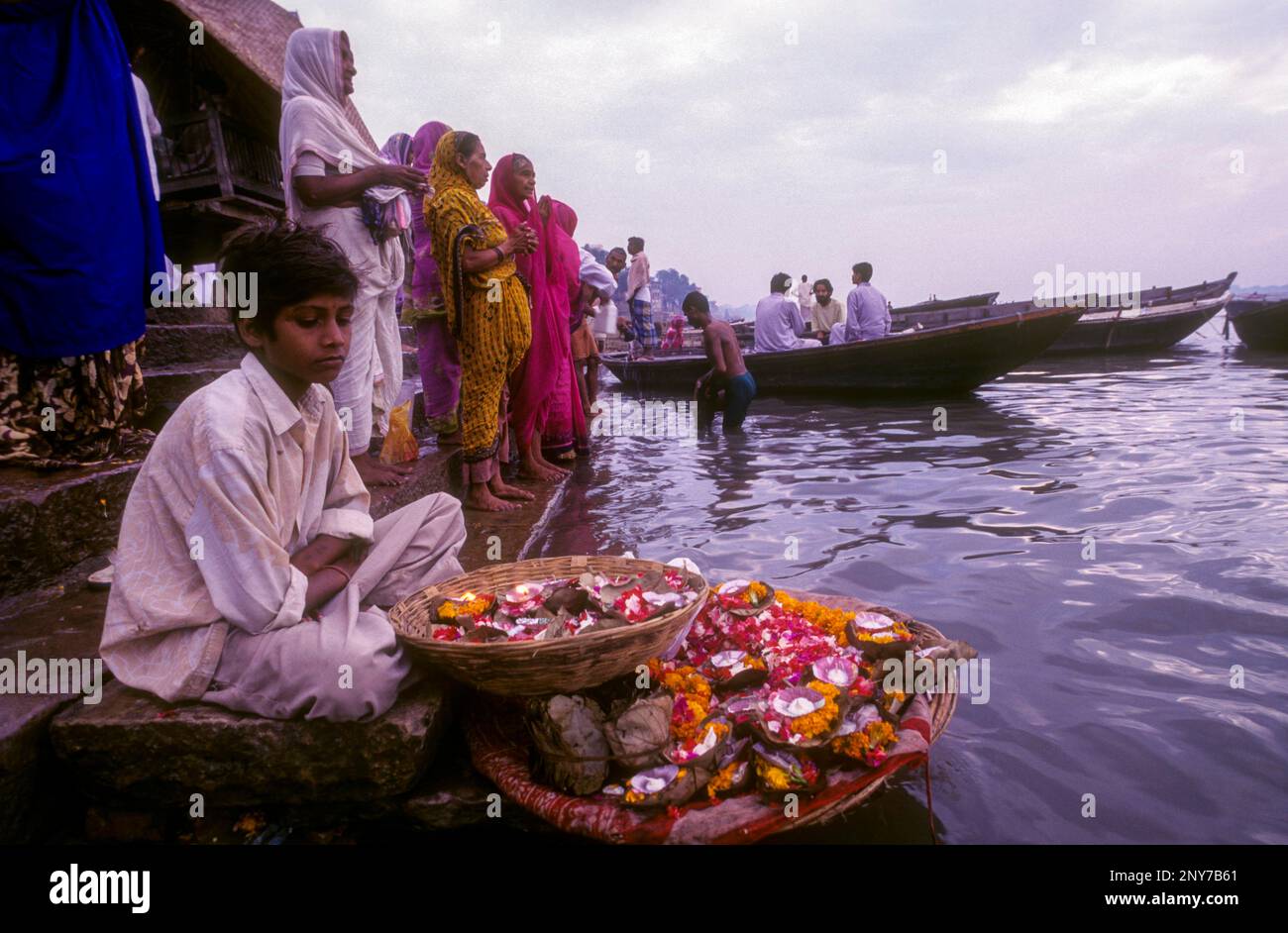 Ein Junge, der mari-Goldblumen verkauft, die in der Fabrik vor dem Fluss Ganga Ganges in Varanasi Benaras, Uttar Pradesh, Indien, Asien, verwendet wurden Stockfoto