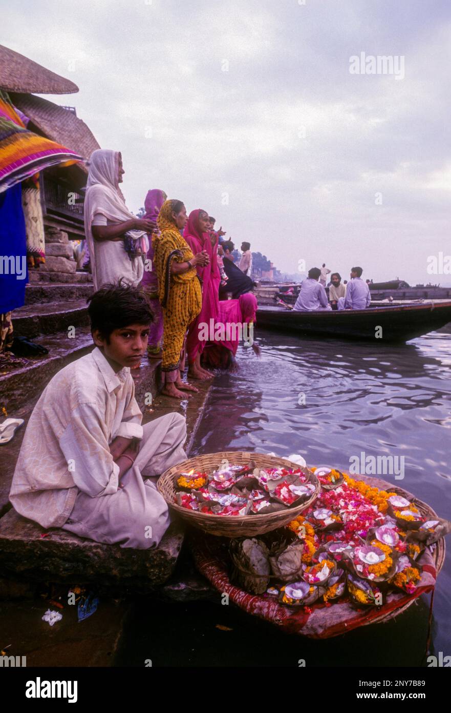 Ein Junge, der mari-Goldblumen verkauft, die in der Fabrik vor dem Fluss Ganga Ganges in Varanasi Benaras, Uttar Pradesh, Indien, Asien, verwendet wurden Stockfoto