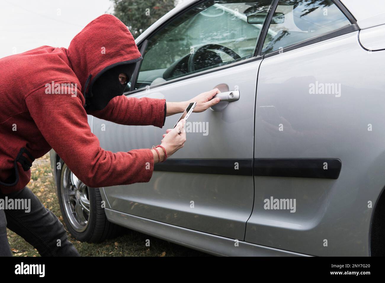 Ein junger Betrüger versucht, das Auto eines anderen zu stehlen, indem er über das Car Link-Anwendungssystem auf einem Smartphone versucht. Fahrzeug mit der mobilen App entriegeln. Männlicher Verbrecher bricht das Stockfoto