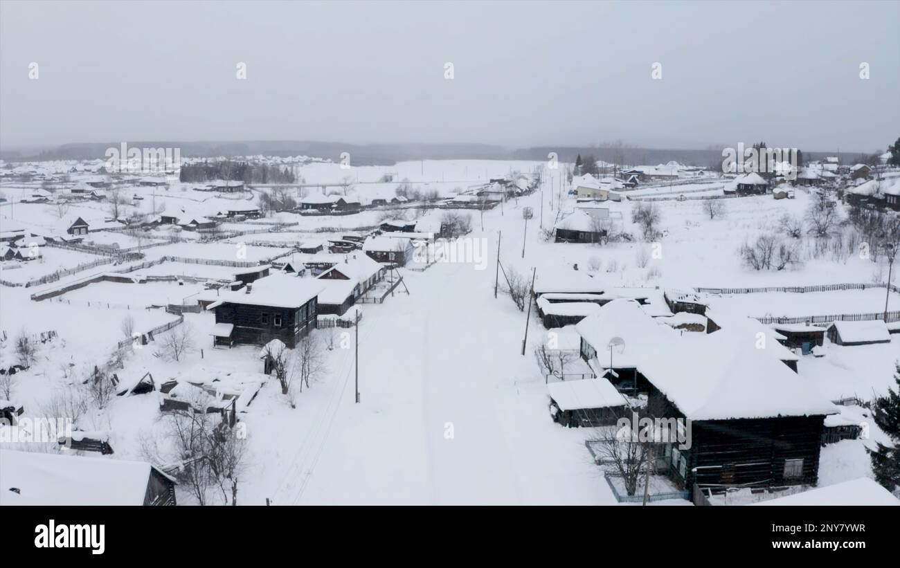 Schneebedeckte Dächer von Holzhäusern aus der Vogelperspektive. Clip. Kleines Winterdorf mit schwerem bewölktem Himmel Stockfoto
