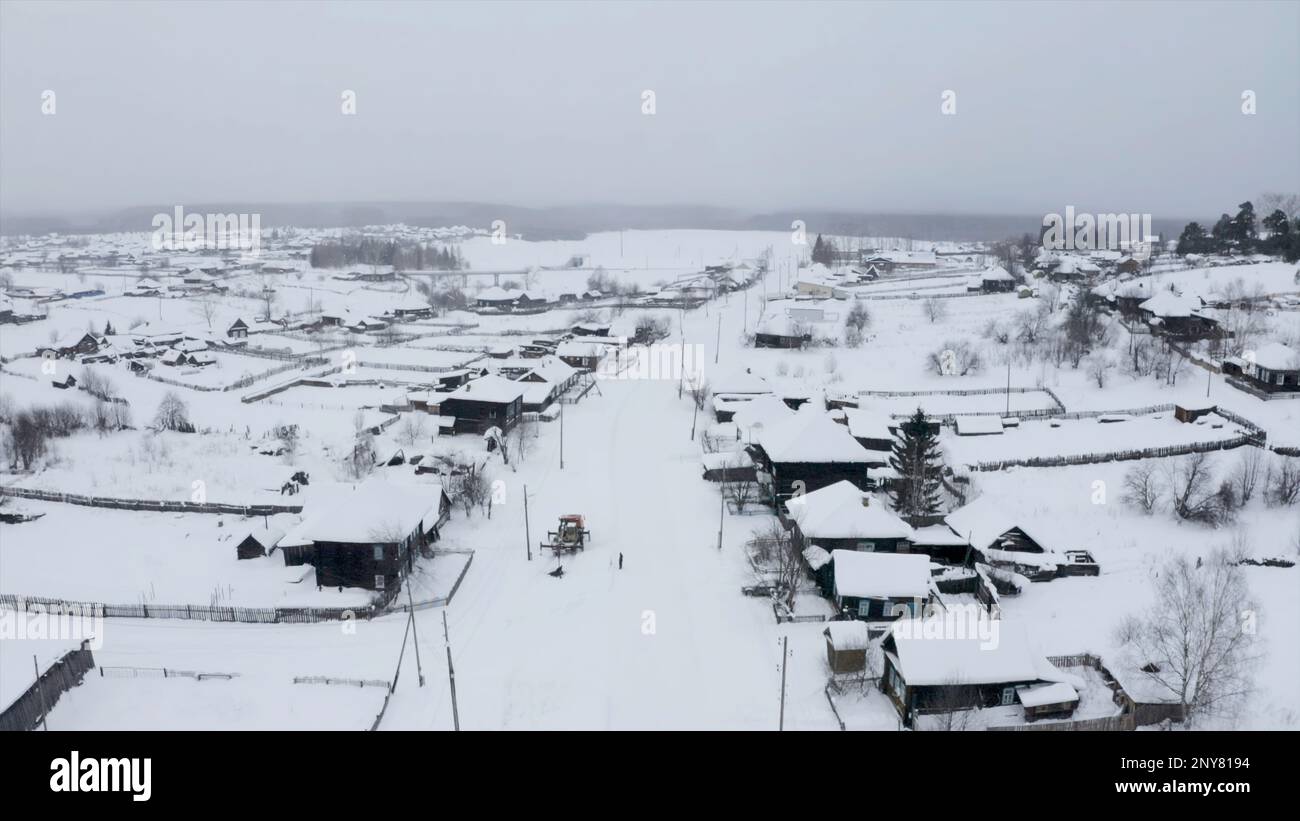 Schneebedeckte Dächer von Holzhäusern aus der Vogelperspektive. Clip. Kleines Winterdorf mit schwerem bewölktem Himmel Stockfoto