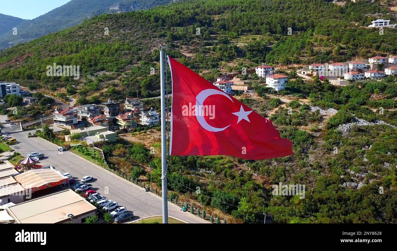 Luftaufnahme einer türkischen Staatsflagge. Clip. Sommergrüne Berge und Vegetation mit Gebäuden Stockfoto