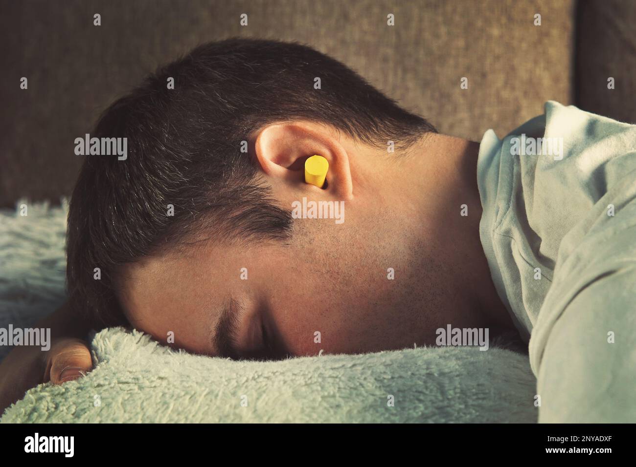 Mann mit Ohrstöpseln liegt im Bett. Tagsüber schlafen. Ruh dich aus, Siesta. Gelbe Ohrstöpsel in den Ohren eines kleinen Jungen, der nachmittags auf der Couch schläft, wenn p Stockfoto