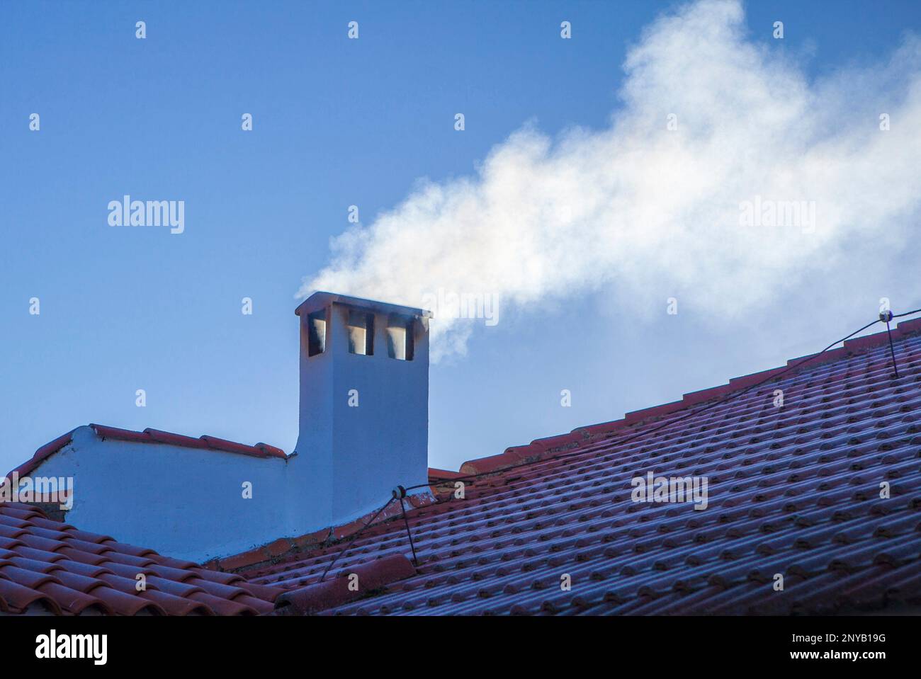 Rauchiger Schornstein auf einem Dach mit Winterfrost. Blauer Himmelshintergrund. Stockfoto