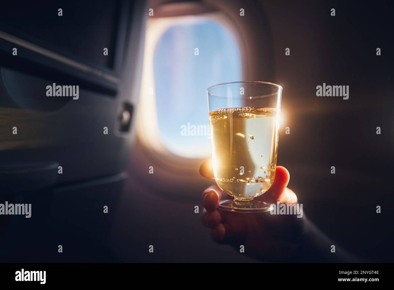Ein Mann, der während des Fluges etwas trinkt. Passagier hält ein Glas Sekt gegen das Flugzeugfenster. Stockfoto