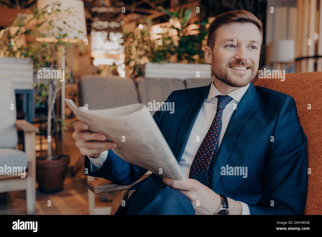 Porträt eines erfolgreichen Jungunternehmers in moderner formeller Kleidung, während er Sektion der Finanzzeitschrift in der Zeitung liest und auf Ordnung wartet Stockfoto