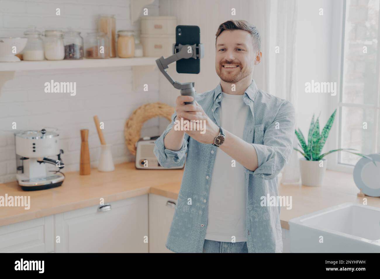 Junger Mann Blogger nimmt Video-Blog auf oder streamt Livestreams mit Smartphone und Gimbal drinnen im Küchenhintergrund. Social-Media-Vlogger-Shooting Stockfoto