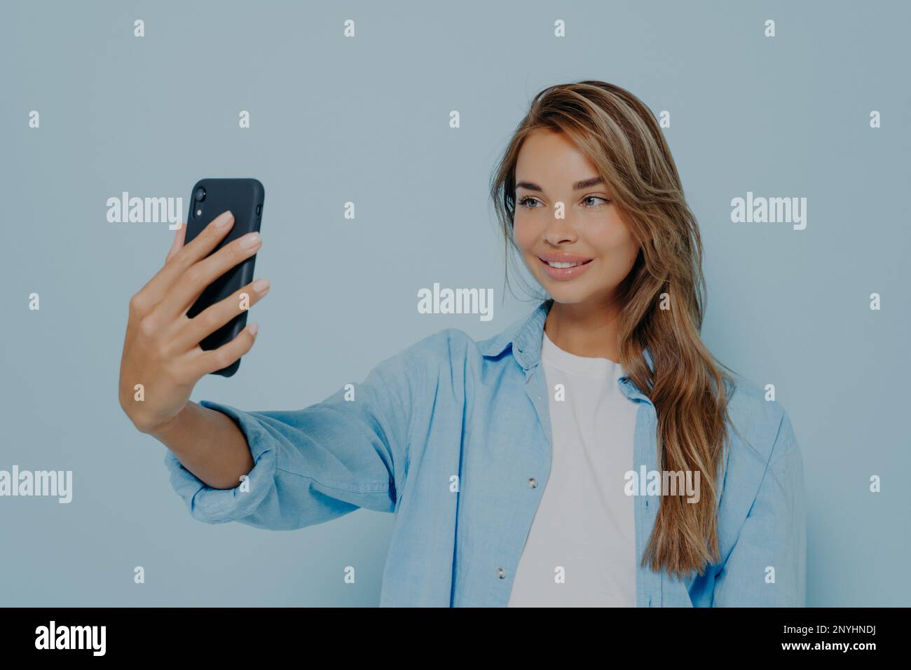 Zeit für Selfie. Eine großartige junge Frau in stilvollen, lässigen Kleidern mit langen, gefärbten Haaren, die auf einem modernen Handy Fotos von sich macht und charmant aussieht Stockfoto