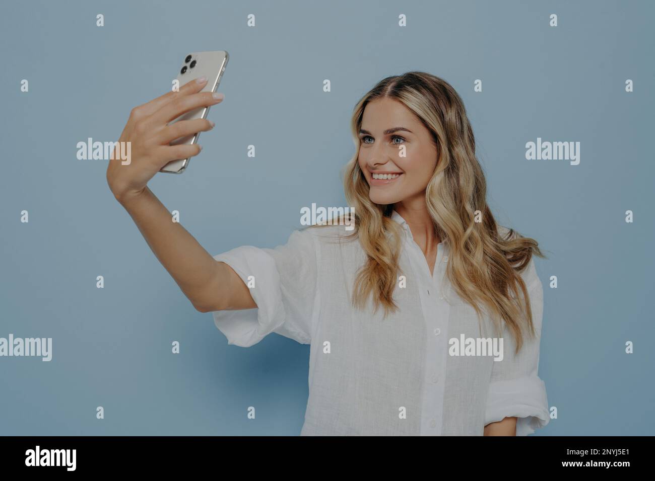 Blondes Teenager-Mädchen macht Selfie auf einem modernen Smartphone für Social-Media-Konten mit einem strahlenden Lächeln, lächelt für die Kamera und teilt Fotos mit ihrer Pommes Frites Stockfoto