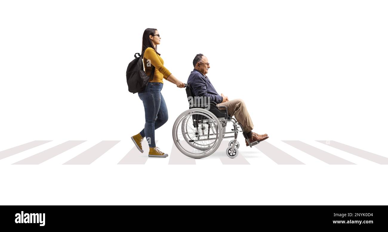 Profilaufnahme über die gesamte Länge einer jungen Frau, die einen erwachsenen Mann im Rollstuhl auf einem Fußgängerübergang schubst, isoliert auf weißem Hintergrund Stockfoto