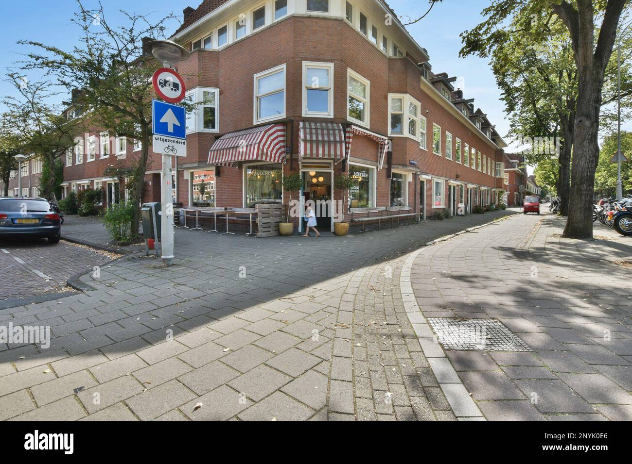 Amsterdam, Niederlande - 10. April 2021: Ein Backsteingebäude an der Seite einer Straße mit Autos, die vor dem Hotel geparkt sind und hinter denen Bäume den Bürgersteig säumen Stockfoto