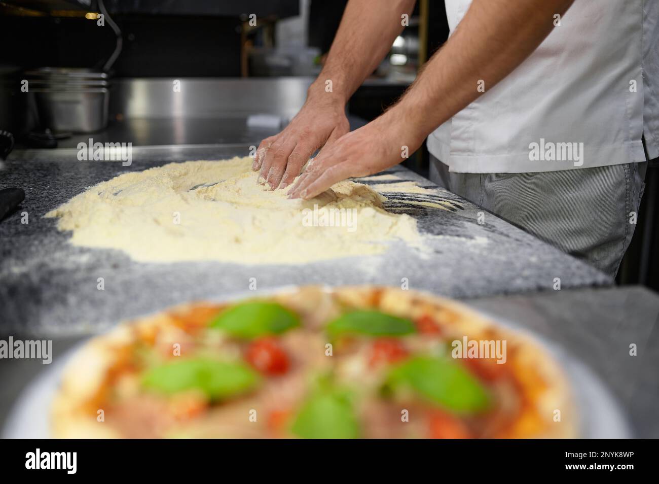 Der Küchenchef mischt Mehl, um Pizzateig zu kneten Stockfoto