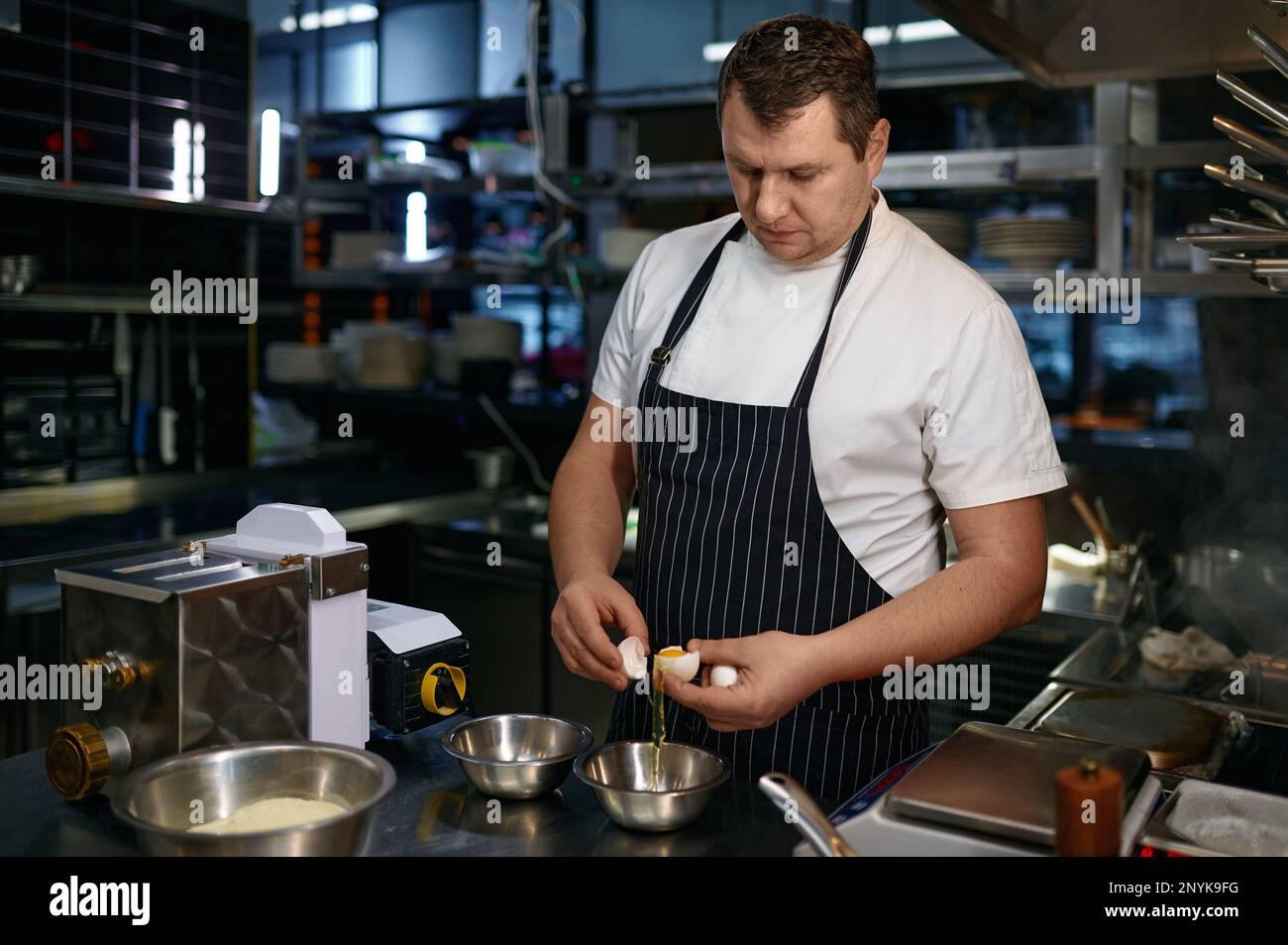 Reifer Koch in der Schürze knackt frische Eier, während er Nudeln kocht Stockfoto