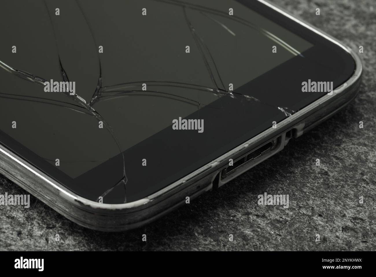 Smartphone mit rissigem Bildschirm auf grauem Steinhintergrund, Nahaufnahme. Gerätereparatur Stockfoto