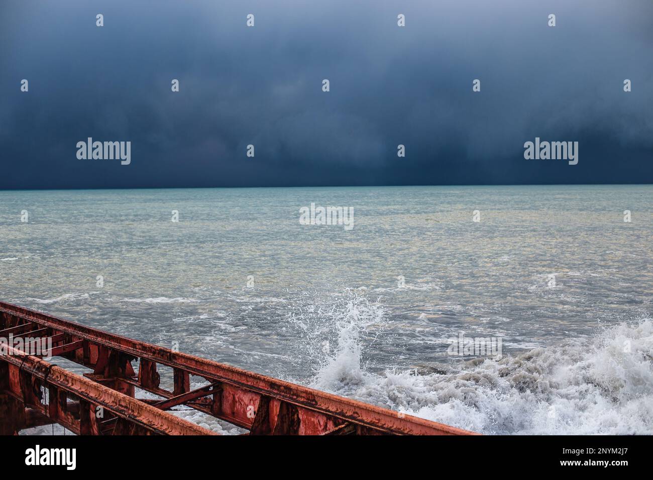 Alter roter Pier und stimmungsvolles stürmisches Meer mit einer satten blauen Farbe von Wasser und Wolken. Minimalistische Sturmlandschaft Stockfoto