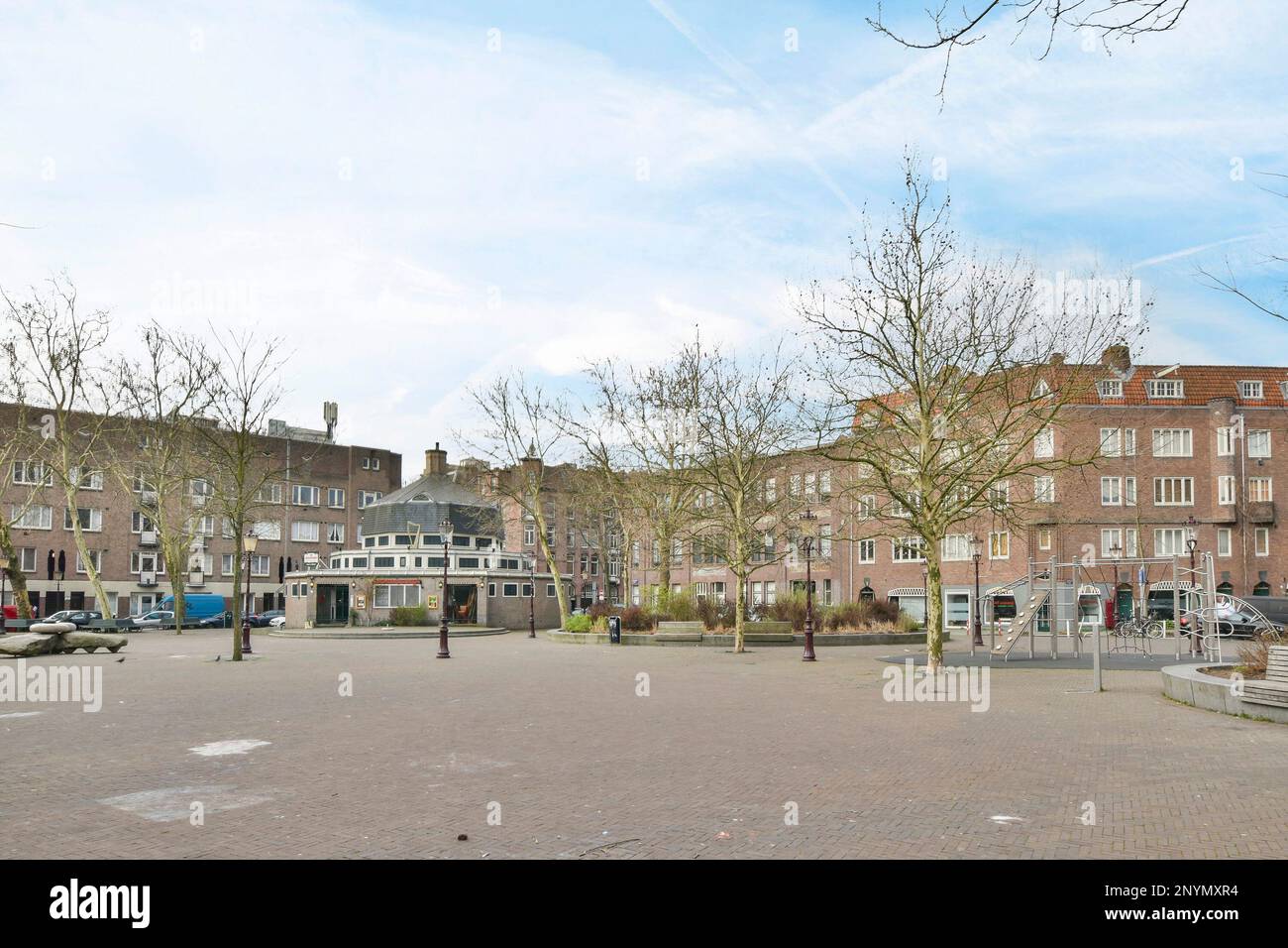 Ein Stadtplatz mit Bäumen und Gebäuden im Hintergrund, an einem sonnigen Tag gibt es einen leeren Parkplatz Stockfoto