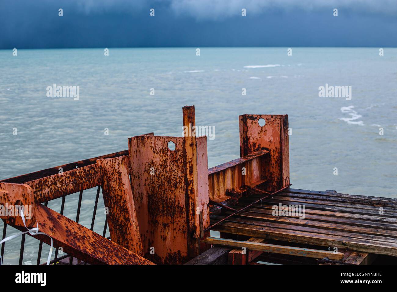 Alter rostiger Pier und stimmungsvolles stürmisches Meer mit einer satten blauen Farbe von Wasser und Wolken. Minimalistische Sturmlandschaft Stockfoto