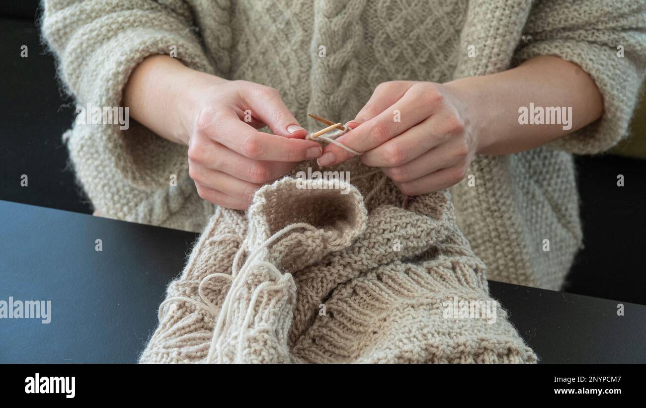 Weibliche Hände stricken in Cocose-up. Mädchen, die sich entspannen und einen warmen Pullover stricken. Stockfoto