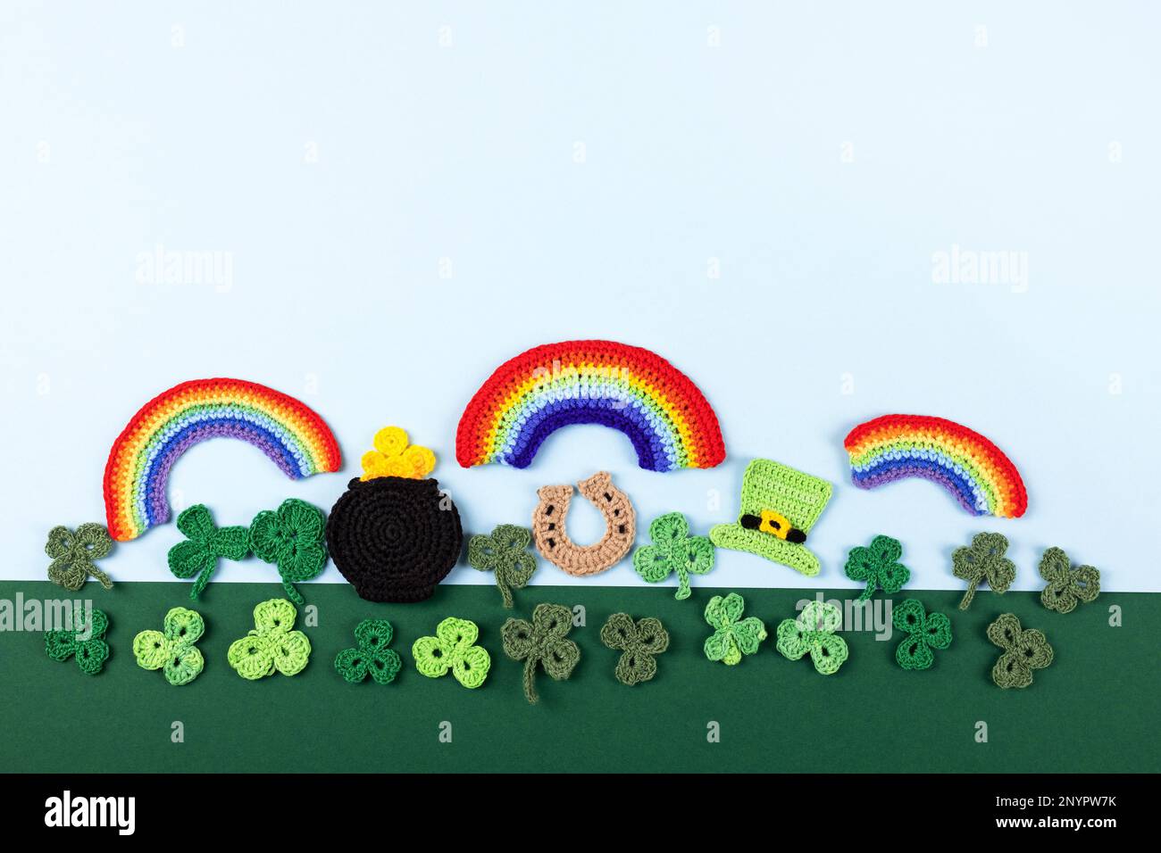 St. Patrick's Day Konzept. Gestrickte Komposition aus grünem Hut, goldenem Topf, Hufeisen, Regenbogen und grünen Shamrocks auf grün-blauem Hintergrund Stockfoto