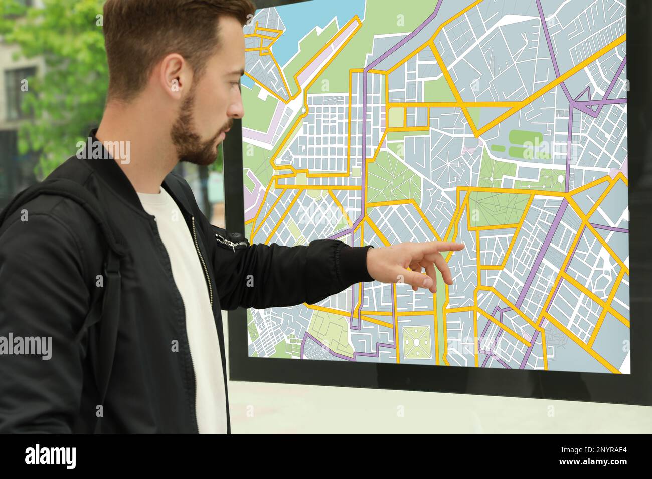 Junger Mann in der Nähe der Karte für öffentliche Verkehrsmittel an der Bushaltestelle, Nahaufnahme Stockfoto