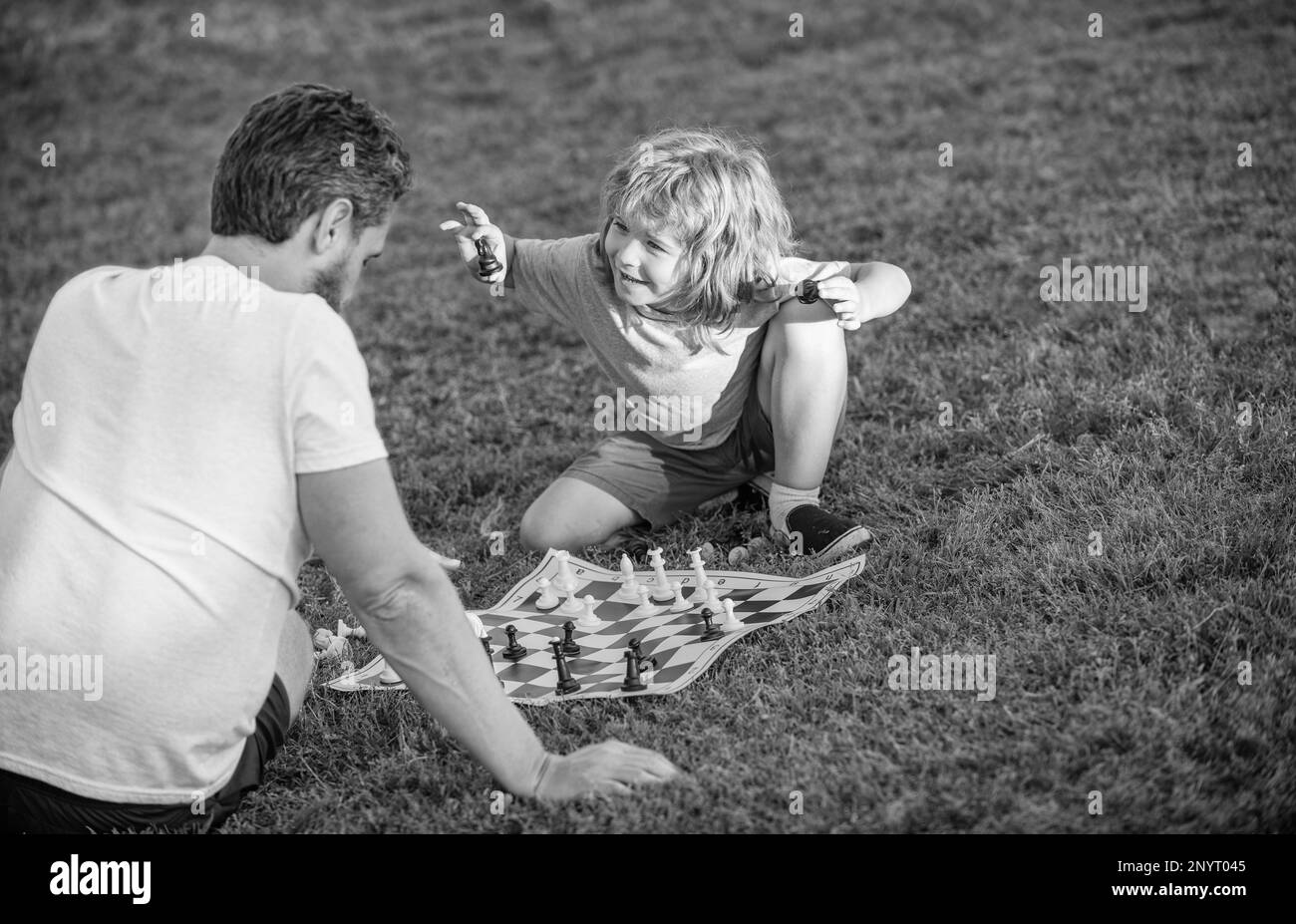 Glückliche Familie von Vater und Sohn, die Schach auf grünem Gras im Park spielen, Schachspiel. Stockfoto