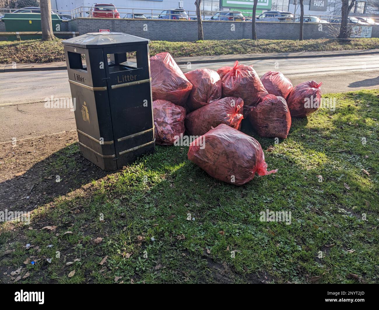 Eine rote Mülltüte, die sich an Einer Straßenecke stapelt und neben Einem Metallbehälter auf ihre Abholung wartet Stockfoto