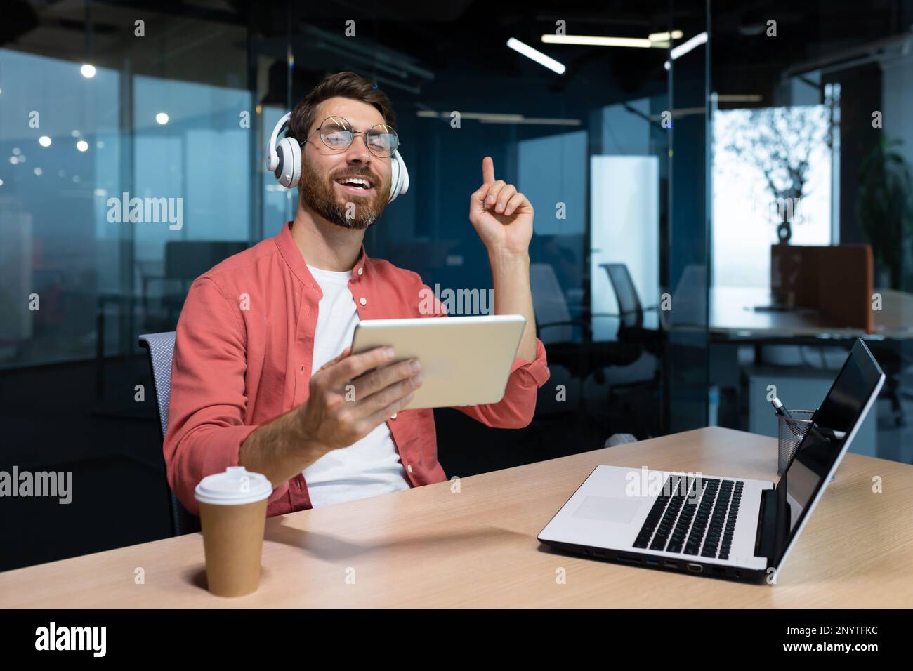 Eine junge Freiberuflerin, Studentin, Programmiererin sitzt mit einem Laptop im Büro, hört Musik über Kopfhörer und hält das Tablet in den Händen. Er schloss die Augen, ruht sich aus, entspannt, tanzt, singt. Stockfoto