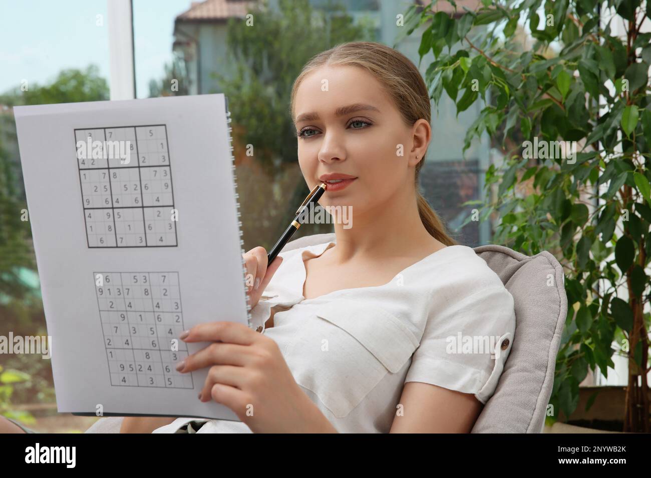 Schöne junge Frau löst Sudoku-Rätsel in der Nähe von Fenstern  Stockfotografie - Alamy