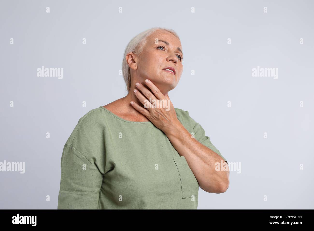 Reife Frau, die sich auf hellgrauem Hintergrund einer Schilddrüsen-Selbstuntersuchung unterzieht Stockfoto