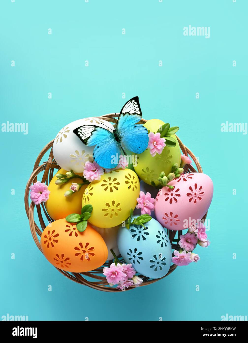 Bunte Ostereier im Korb und Blumen auf blauem Hintergrund. Pastellfarbene Ostereier Stockfoto