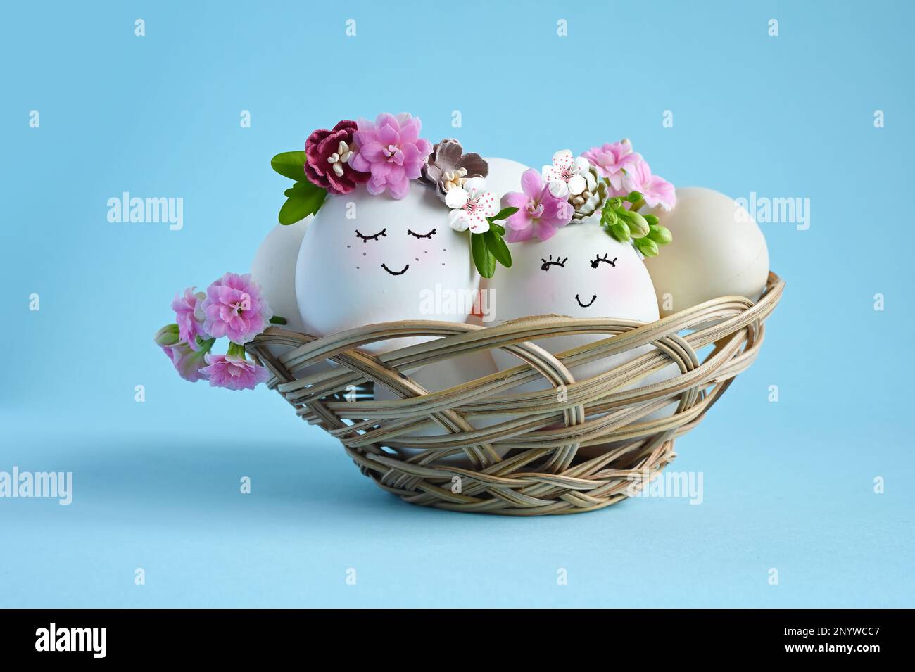 Natürliche Eier mit gezogenem, lächelndem Gesicht in süßer Blumenkrone auf blauem Hintergrund. Frohe Ostern. Stockfoto