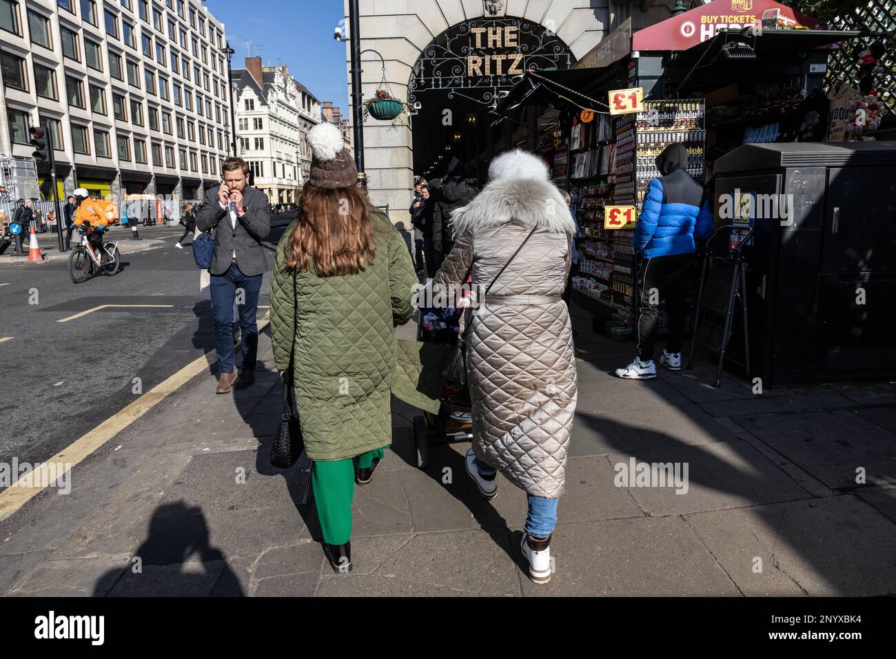 Zwei Damen in gesteppten Bettdecken mit Rautenmuster, die vor dem Ritz Hotel in London, England, Großbritannien entlang des Piccadilly spazieren Stockfoto