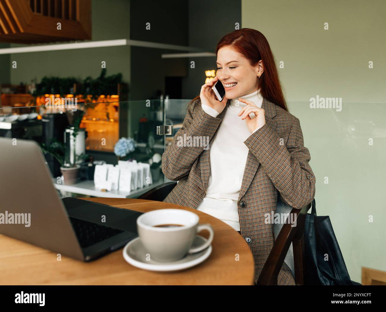 Fröhliche Rothaarige, die telefoniert, während sie in einem Café sitzt Stockfoto