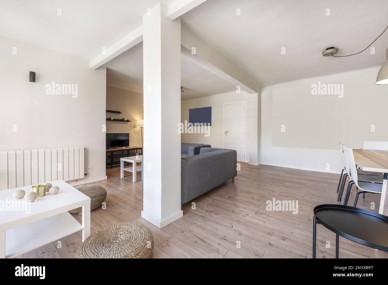 Wohnzimmer einer Ferienmietwohnung mit Kastanienholzböden, natürlichen Faserpasteten, grauen Stoffsofas und einem weißen quadratischen Couchtisch Stockfoto