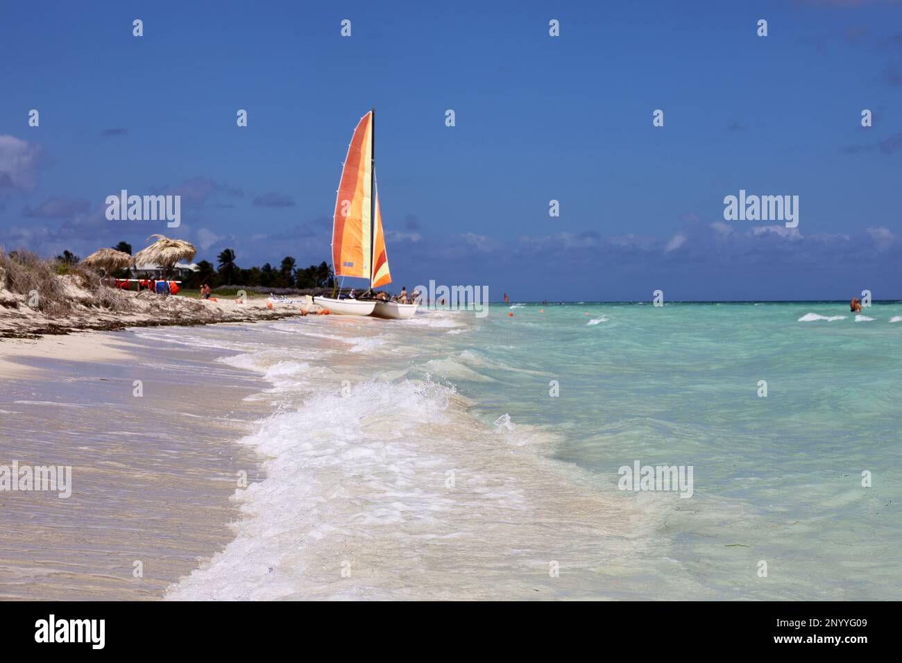 Blick von den Meereswellen bis hin zu Segelbooten und schwimmenden Menschen. Wassersport und Urlaub an einem Strand karibischer Inseln Stockfoto