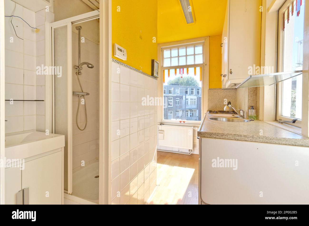 Ein Badezimmer mit gelben Wänden und weißen Fliesen an der Wand, zusammen mit einer begehbaren Duschkabine daneben Stockfoto