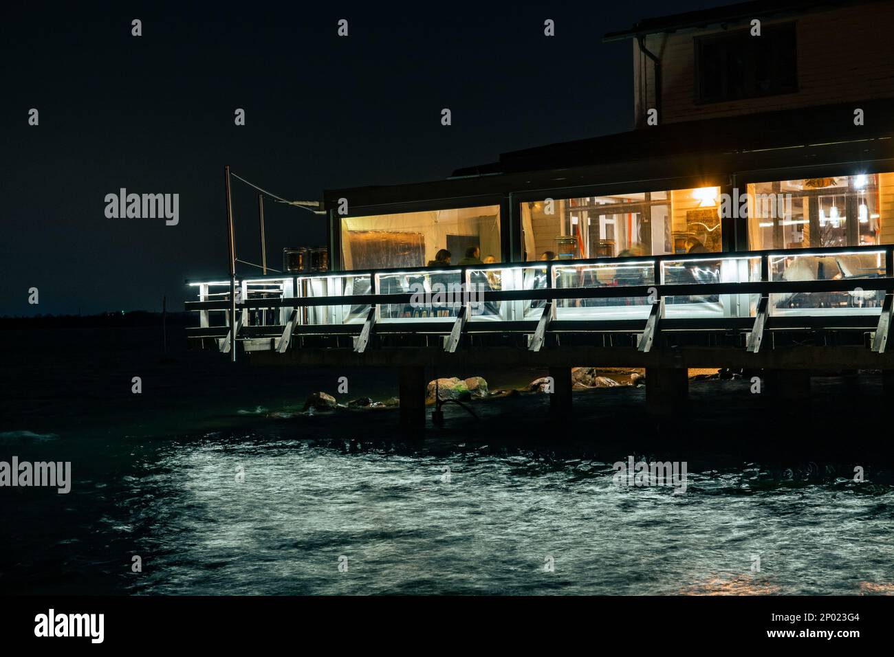 Es gibt ein italienisches Restaurant, das von außen sichtbar ist. Um das Restaurant herum ist Wasser und es ist sehr dunkel. Stockfoto